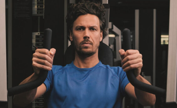 Ein Mann sitzt auf einer Maschine im Fitnessstudio und trainiert seine Muskeln.
