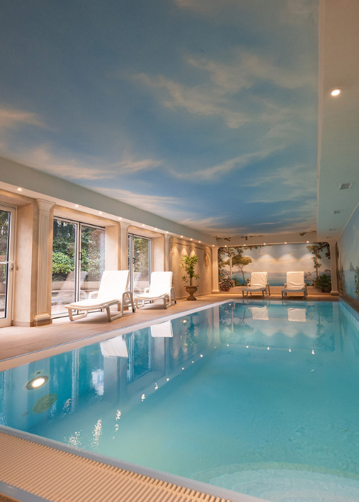 Weitläufiges Hallenbad, dessen Wand mit einem blauen Himmel gestaltet ist, ideal für Erholung und Spaß.