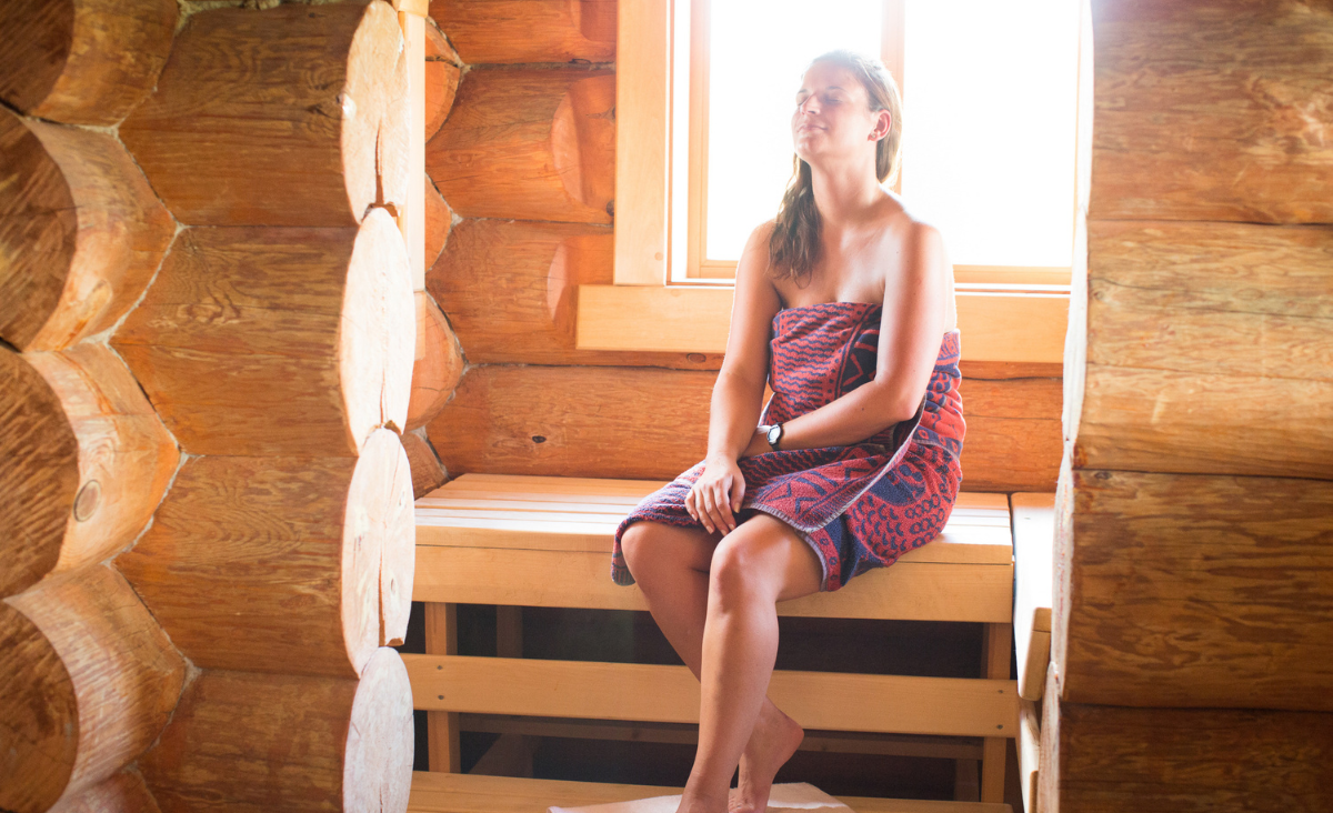Eine Frau sitzt entspannt in einer Sauna und genießt die wohlige Wärme und Ruhe.