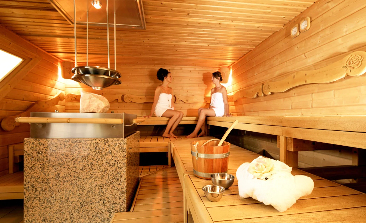 Zwei Frauen relaxen in einem Saunaraum und genießen die wohltuende Hitze.