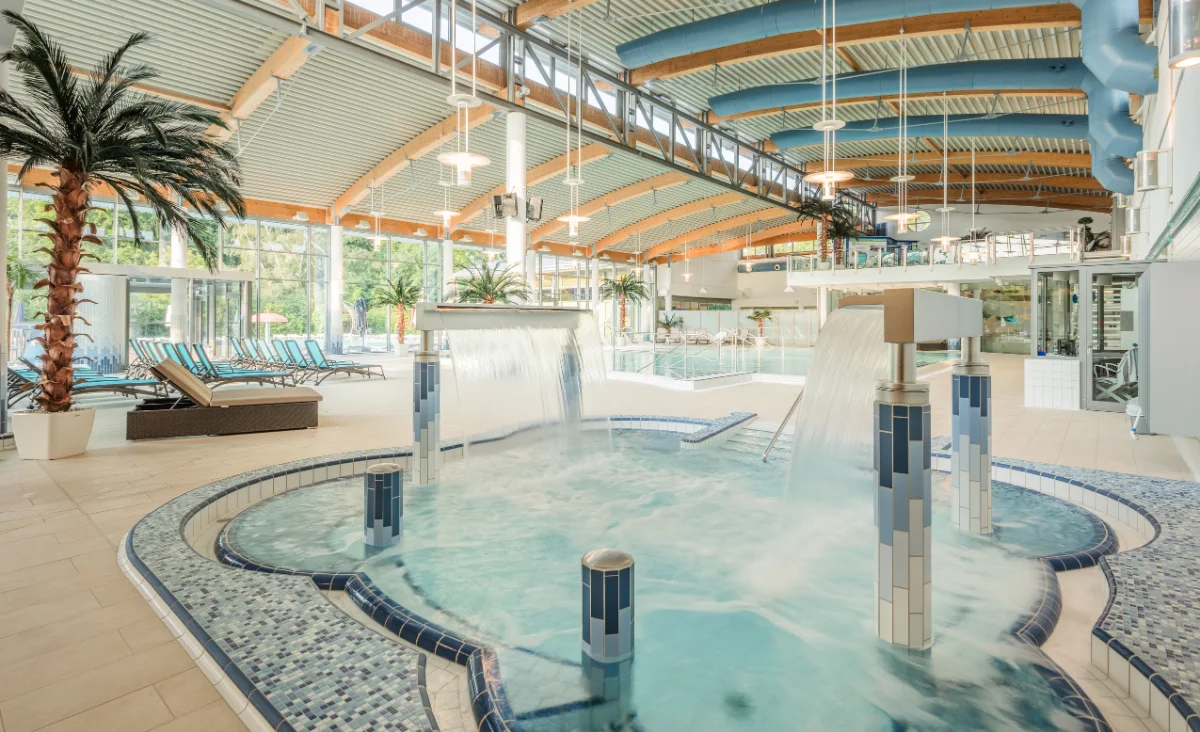 Innenpool mit großem Wasserfall, umgeben von modernen Liegen und Pflanzen.