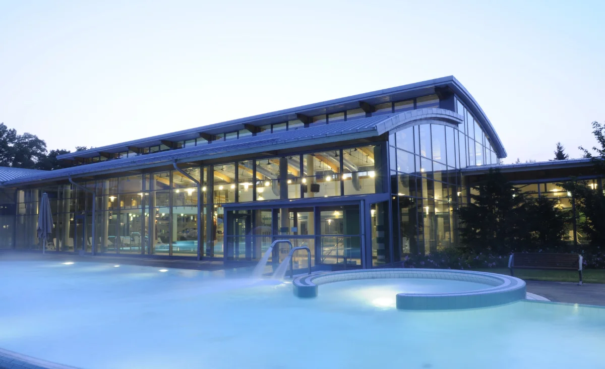 Ein großes Glasgebäude mit einem Schwimmbad im Vordergrund.