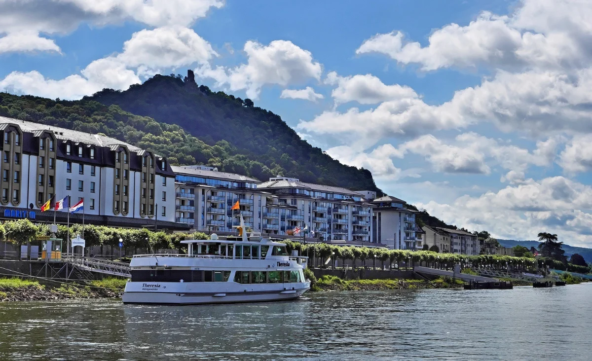 Ein Boot navigiert den Fluss, mit Bergen, die die Landschaft im Hintergrund prägen.