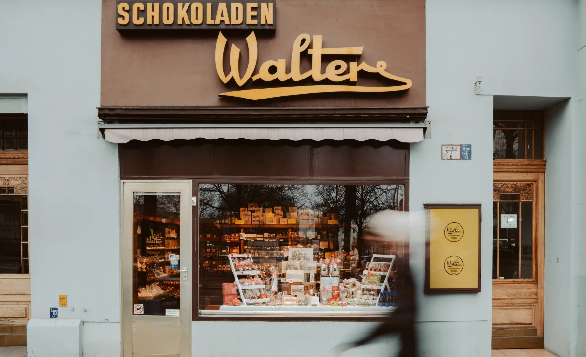 Person geht an einem Geschäft mit dem Schild "Schokoladen" vorbei, das Gutscheine für die Walter Confiserie bewirbt.