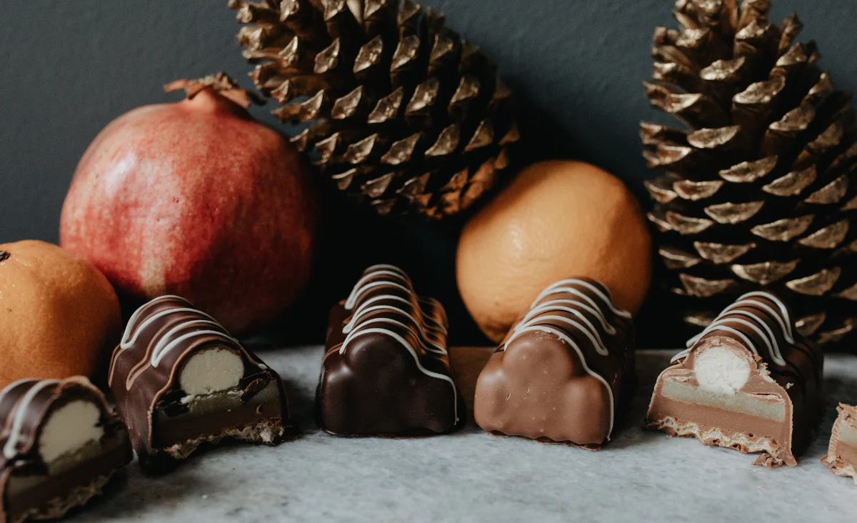 Schokoladeneingehüllte Orangen und Tannenzapfen auf einem rustikalen Holzbrett, dekorativ für die Adventszeit.