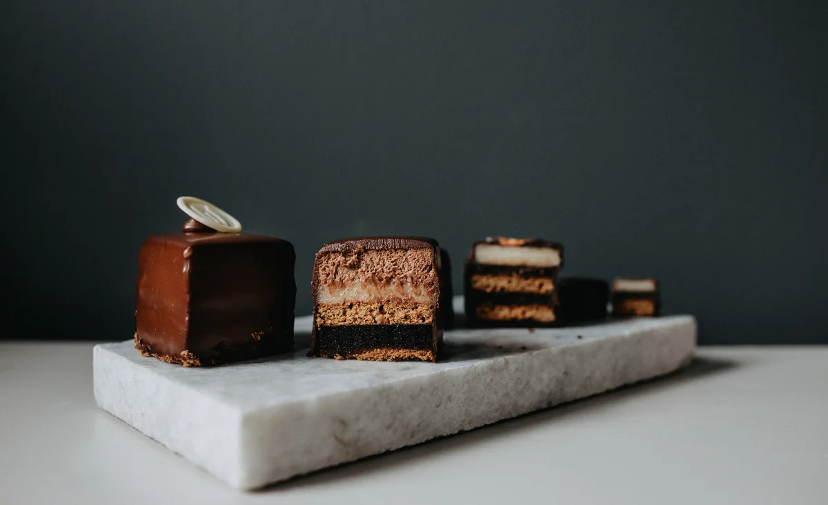 Vier verschiedene Desserts auf einem Marmorbrett, darunter Pralinen und Schokoladen, präsentiert von Walter Confiserie Berlin.