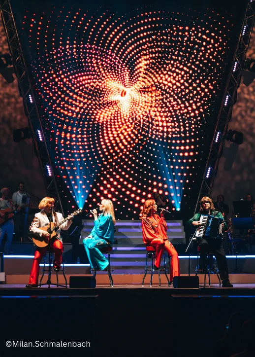 Auf der Bühne stehen mehrere Personen vor einem großen Bühnenhintergrund während der ABBAMANIA THE SHOW in Berlin.