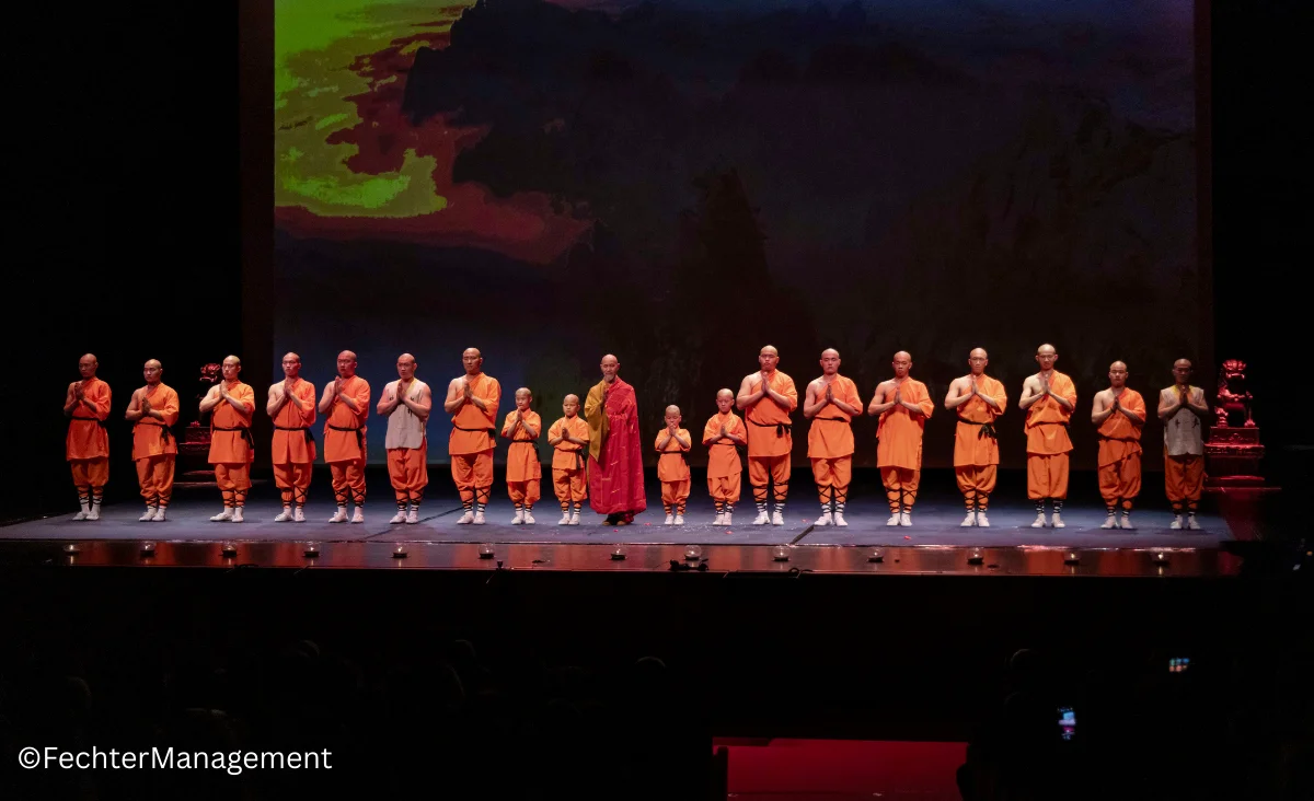 Eine Gruppe von Mönchen auf der Bühne mit einem großen Bildschirm im Hintergrund.