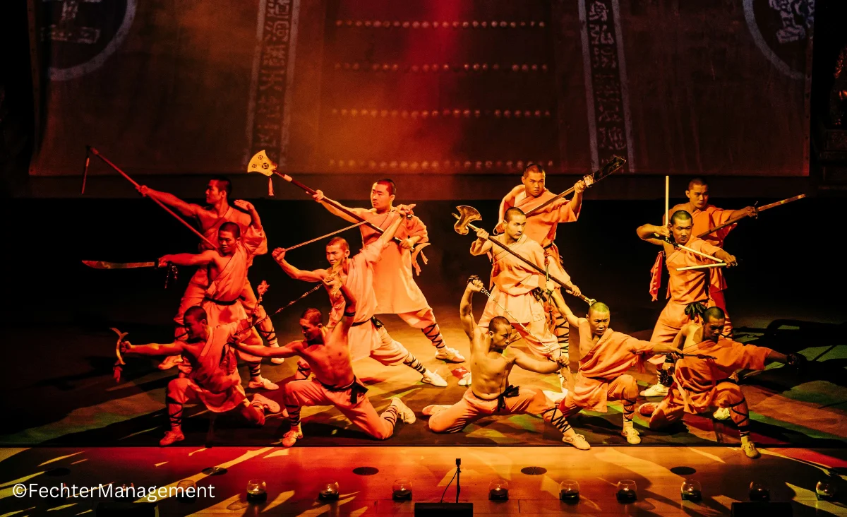 Eine Gruppe von Menschen in traditionellen Kostümen steht auf der Bühne und präsentiert eine kulturelle Darbietung.