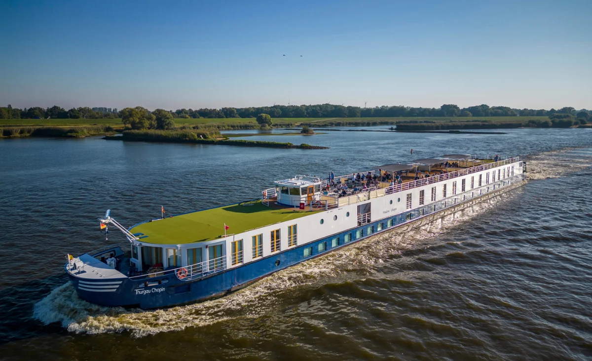 Ein großes blau-weißes Boot-MS Thurgau Chopin - fährt gemächlich einen Fluss entlang, ideal für eine 8-tägige Flusskreuzfahrt für zwei.