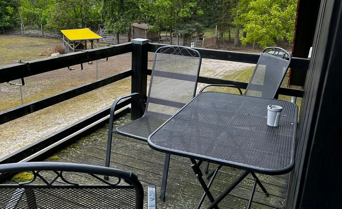 Balkon mit schwarzem Metalltisch und drei passenden Stühlen mit Netzbespannung und einem weißen Becher auf dem Tisch
