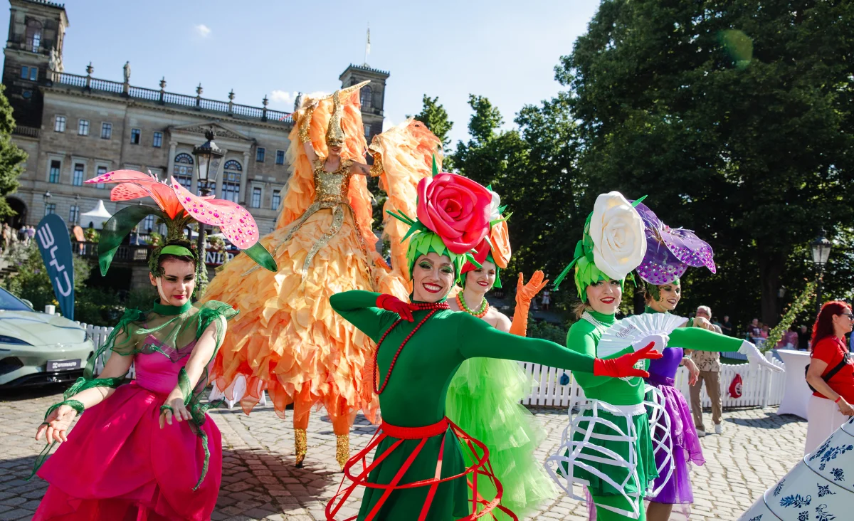 Mehrere als bunte Blumen und eine große orangefarbene Blüte verkleidete Personen tanzen vor dem Dresdner Schloss bei der Dresdner Schloessernacht.