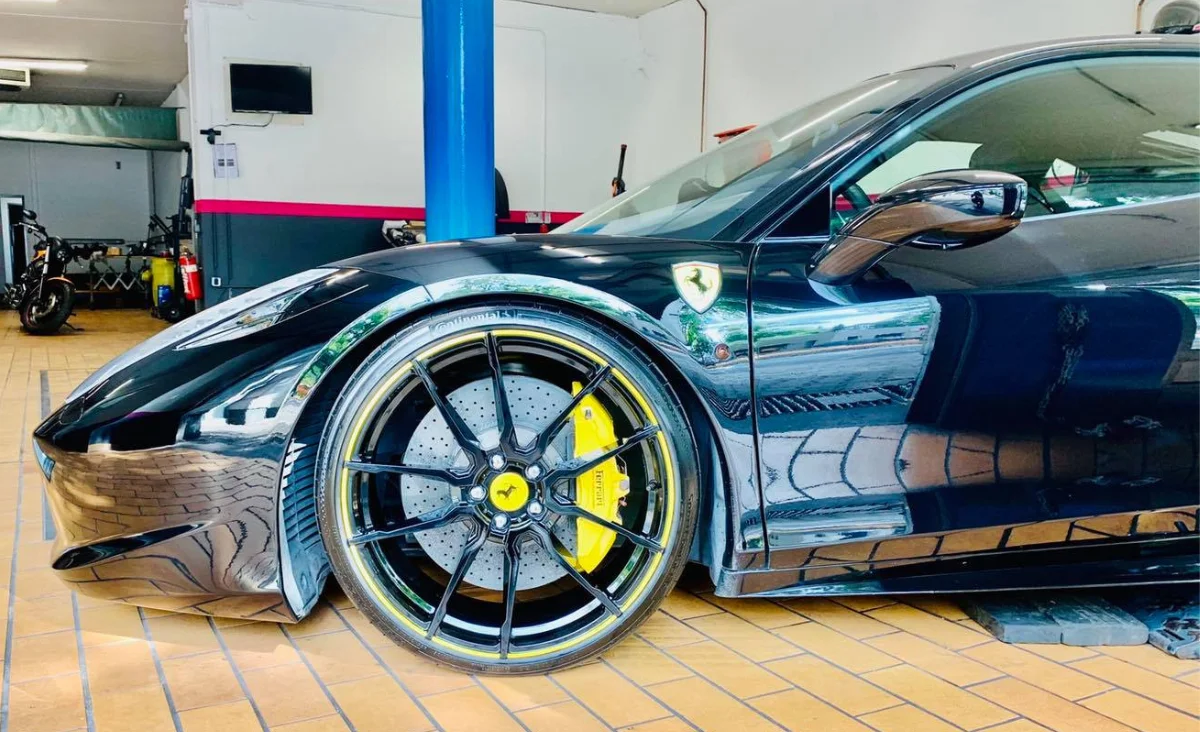 Nahaufnahme eines schwarzen Sportwagens mit gelben Bremsen und Ferrari-Logo in einer Autopflegewerkstatt