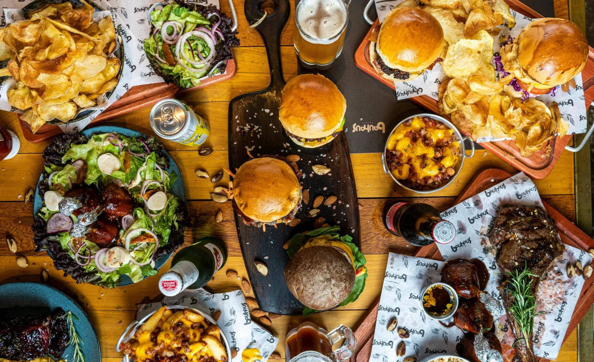 Verschiedene Burger, Pommeschips, Salate und Getränke auf einem Holztisch beim Street Food Festival Zehlendorf