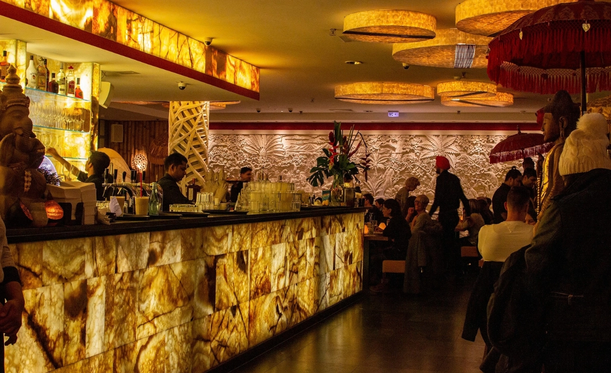 Innenraum eines Restaurants mit beleuchtetem Tresen aus Marmoroptik, mehreren Gästen an Tischen und asiatisch inspirierten Dekorationselementen wie Statuen und Lampions