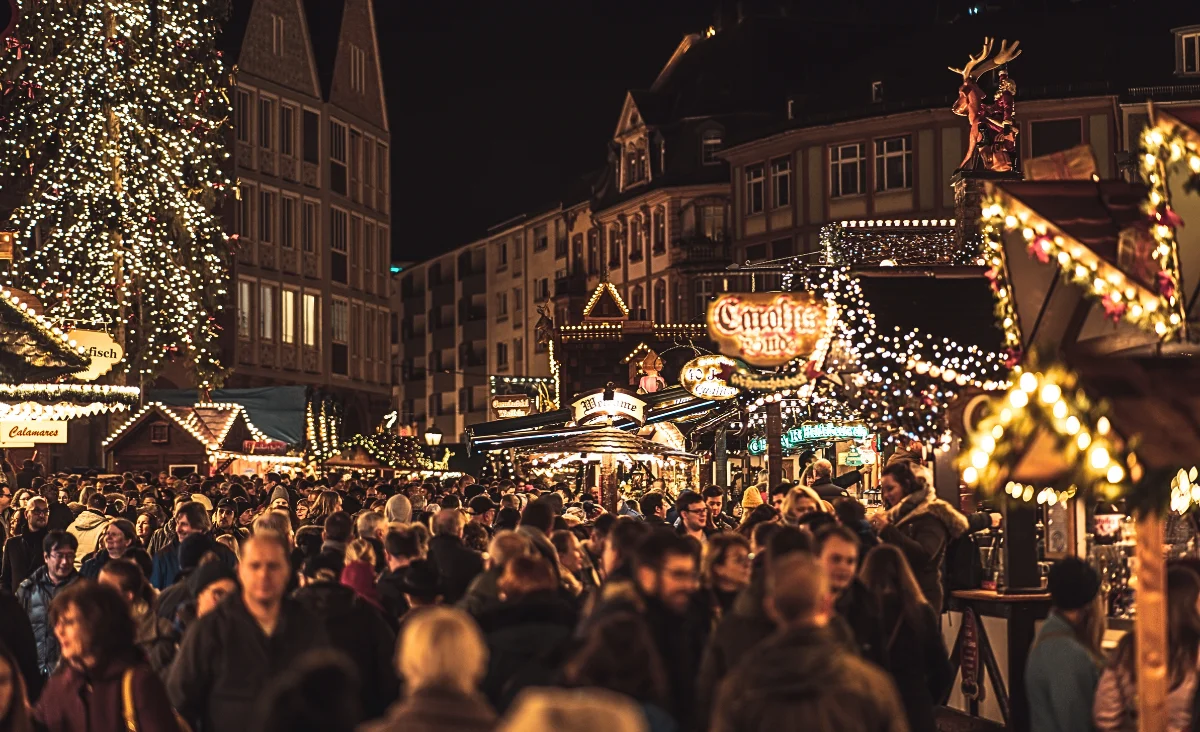 Weihnachtsmarkt mit beleuchteten Ständen, Weihnachtsbaum und Karussell, viele Besucher in Winterkleidung