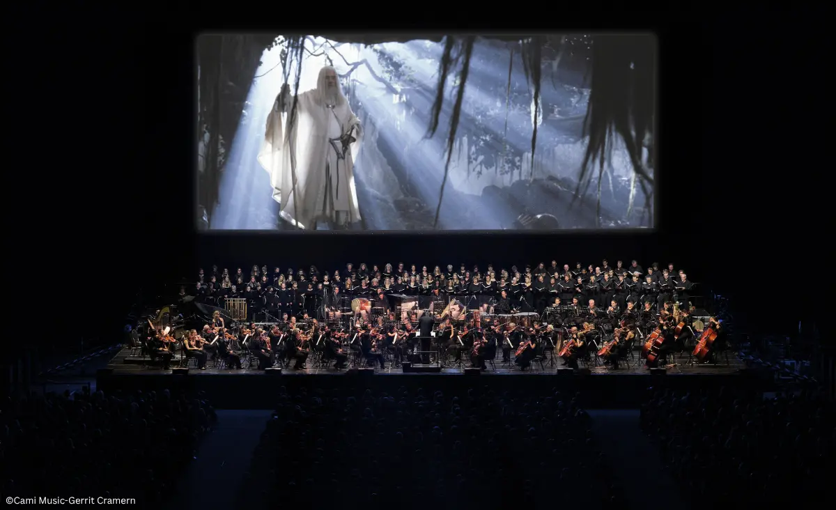 Chor auf der Bühne vor Leinwand mit Projektion einer Szene mit Gandalf in weißem Gewand im Waldlicht.