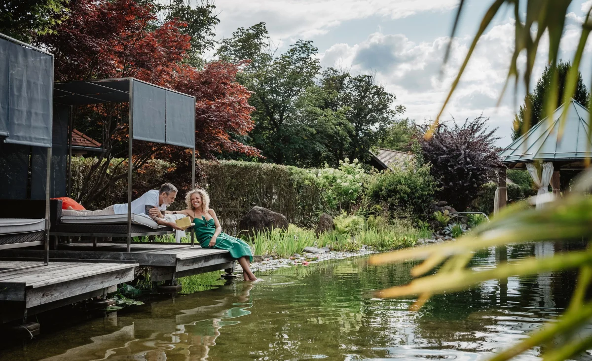 Paar entspannt am idyllischen Naturbadeweiher im Hotel Bodenmaiser Hof auf dem Holzsteg im Grünen