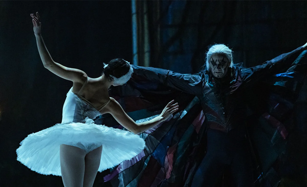 Ballerina in weißem Tutu und Tänzer mit schwarzem Kostüm und dramatischem Gesichtsschmuck in einer Szene aus Schwanensee